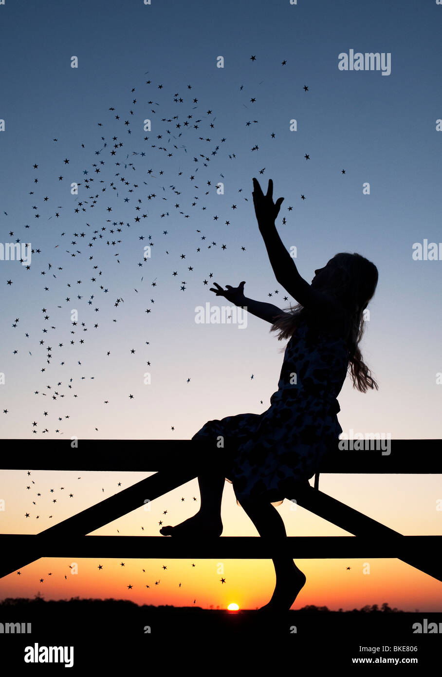 Young Girl having fun with stars sitting on a gate at sunset. Silhouette Stock Photo