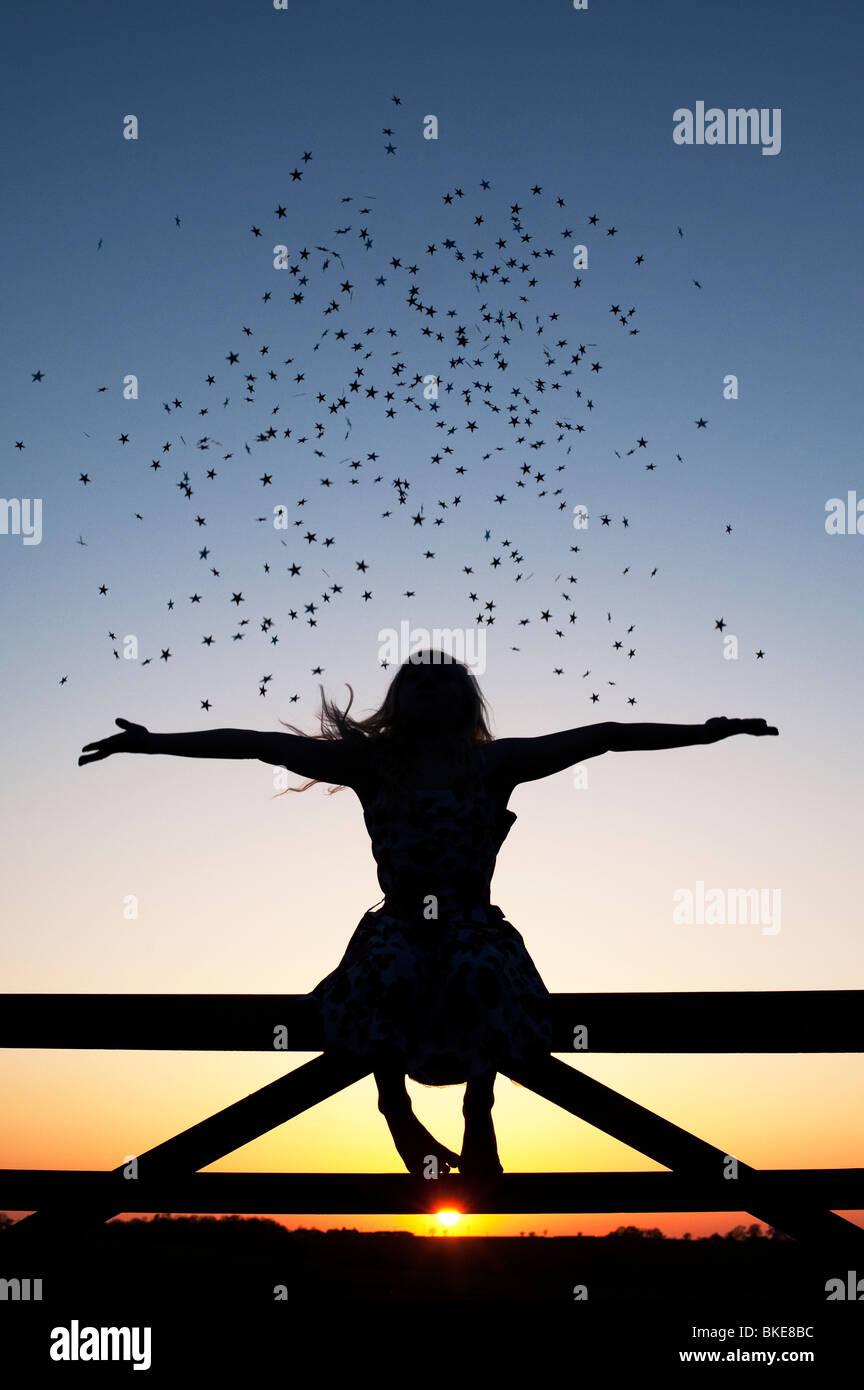 Young Girl having fun with stars sitting on a gate at sunset. Silhouette Stock Photo