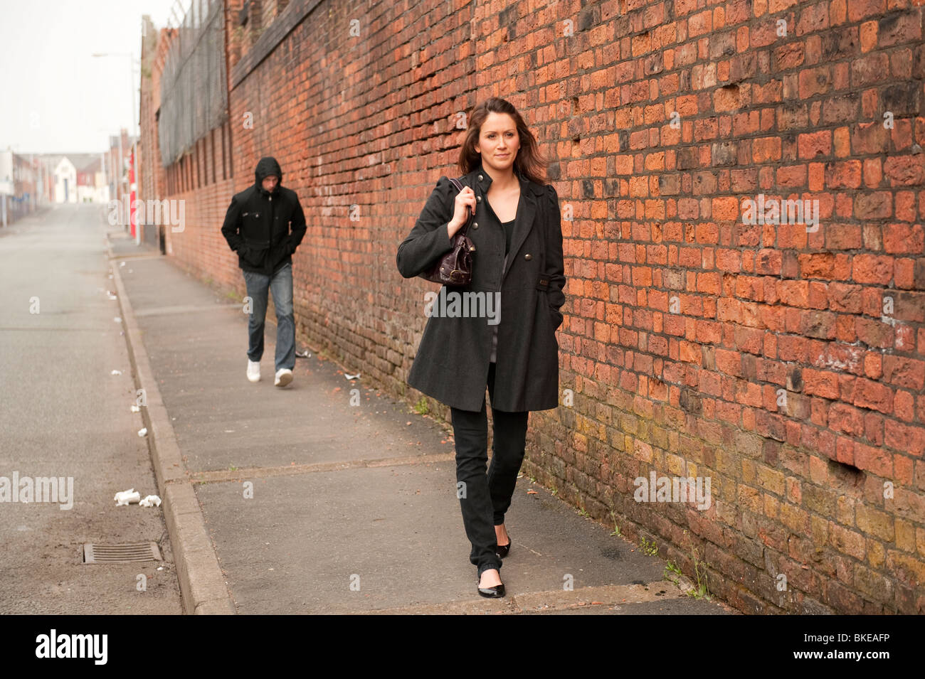 Lone woman walking along street with handbag and thug / criminal in ...