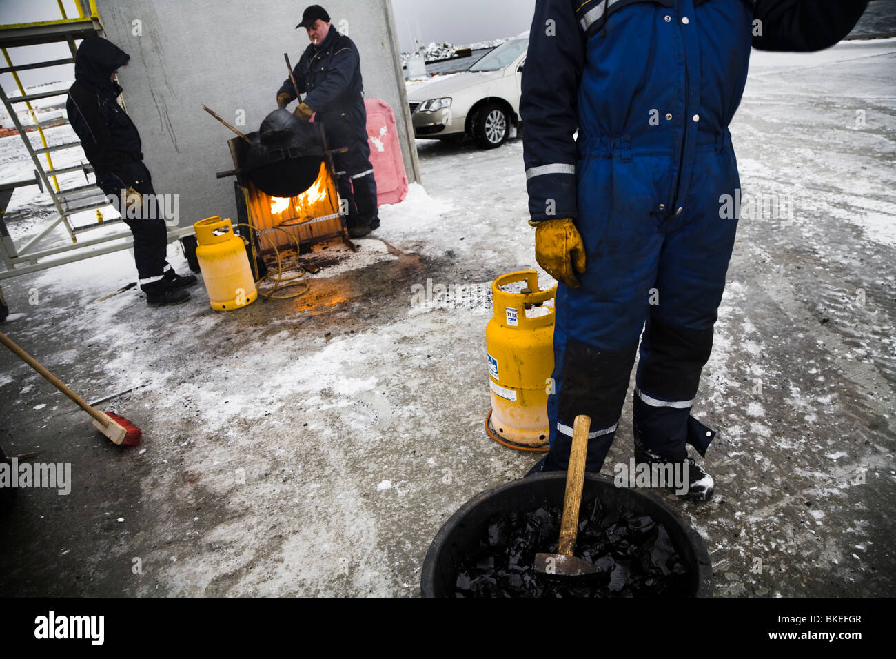 Men working at Vopnafjordur harbour, East Iceland. They are melting tar which is used to seal the concrete joints of the..... Stock Photo