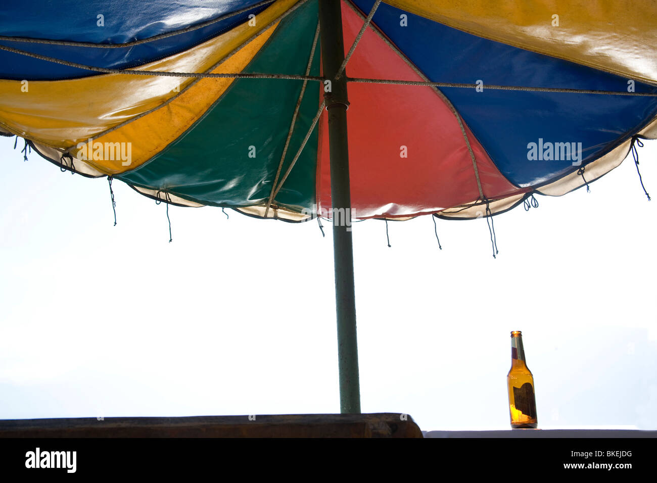 A colourful sun umbrella and an empty beer bottle on a table in a