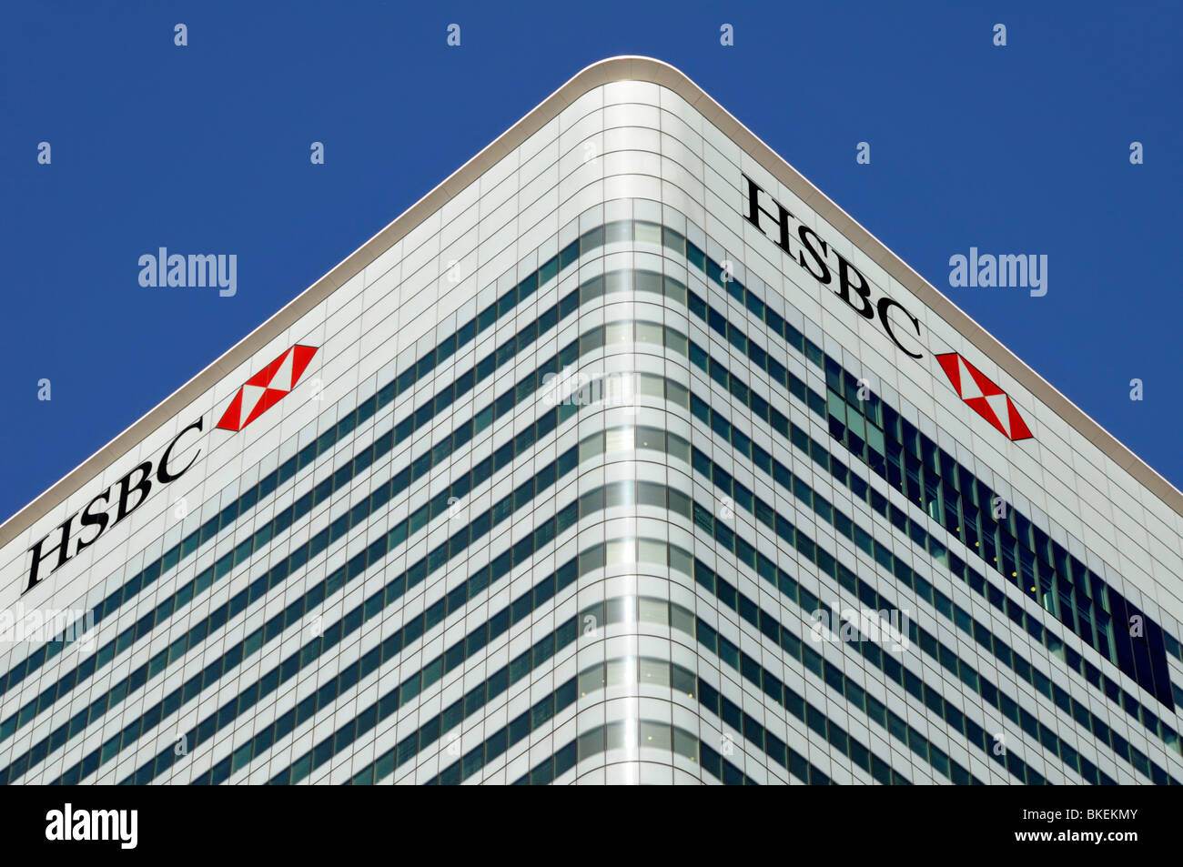 Blue sky corner view of cladding & windows to roof level HSBC bank logo signs at London Docklands Canary Wharf HQ building Tower Hamlets England UK Stock Photo