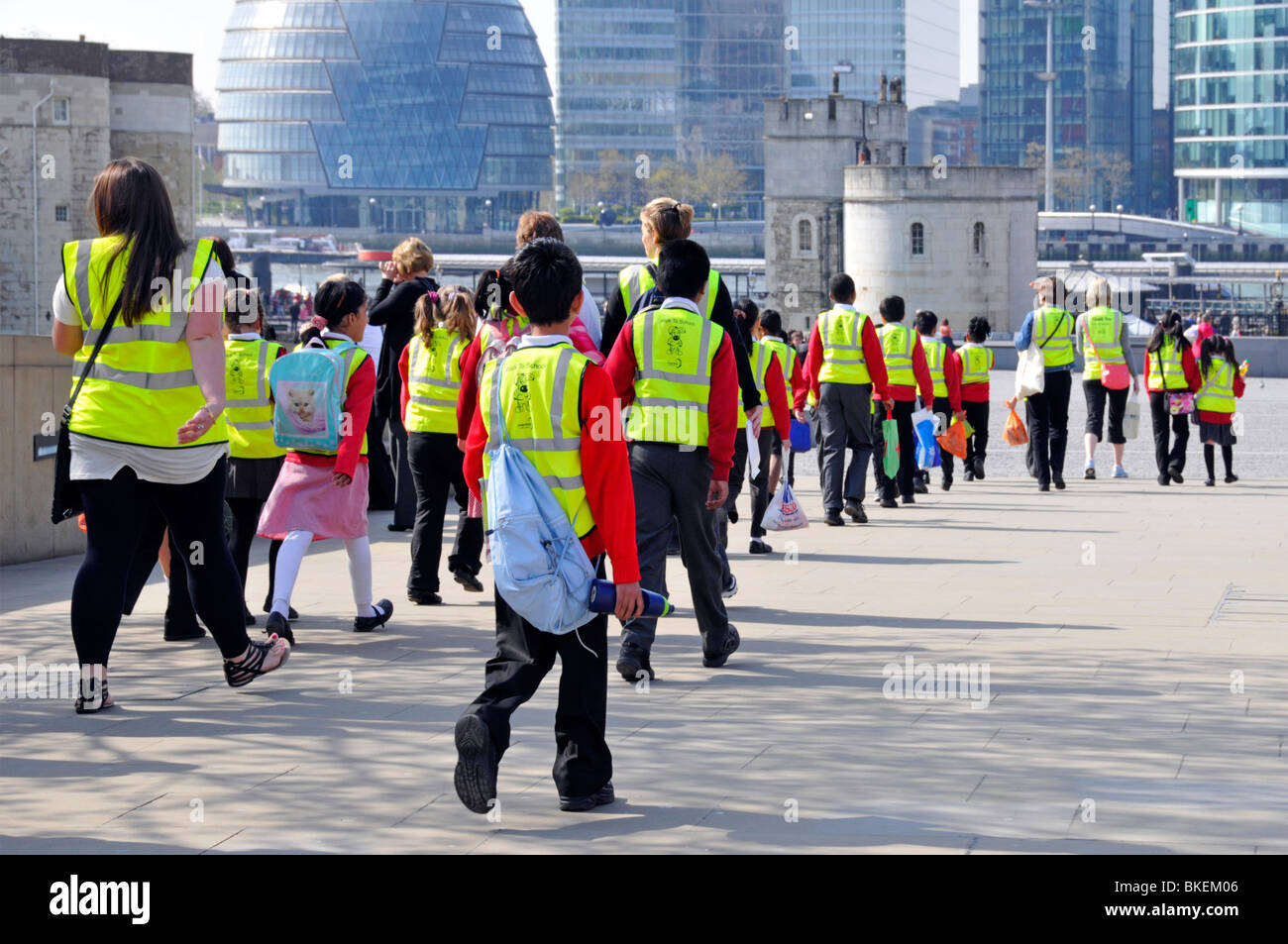 Back view of school trip children & adults wearing high visibility vest clothing on education outing walking towards The Tower of London England UK Stock Photo