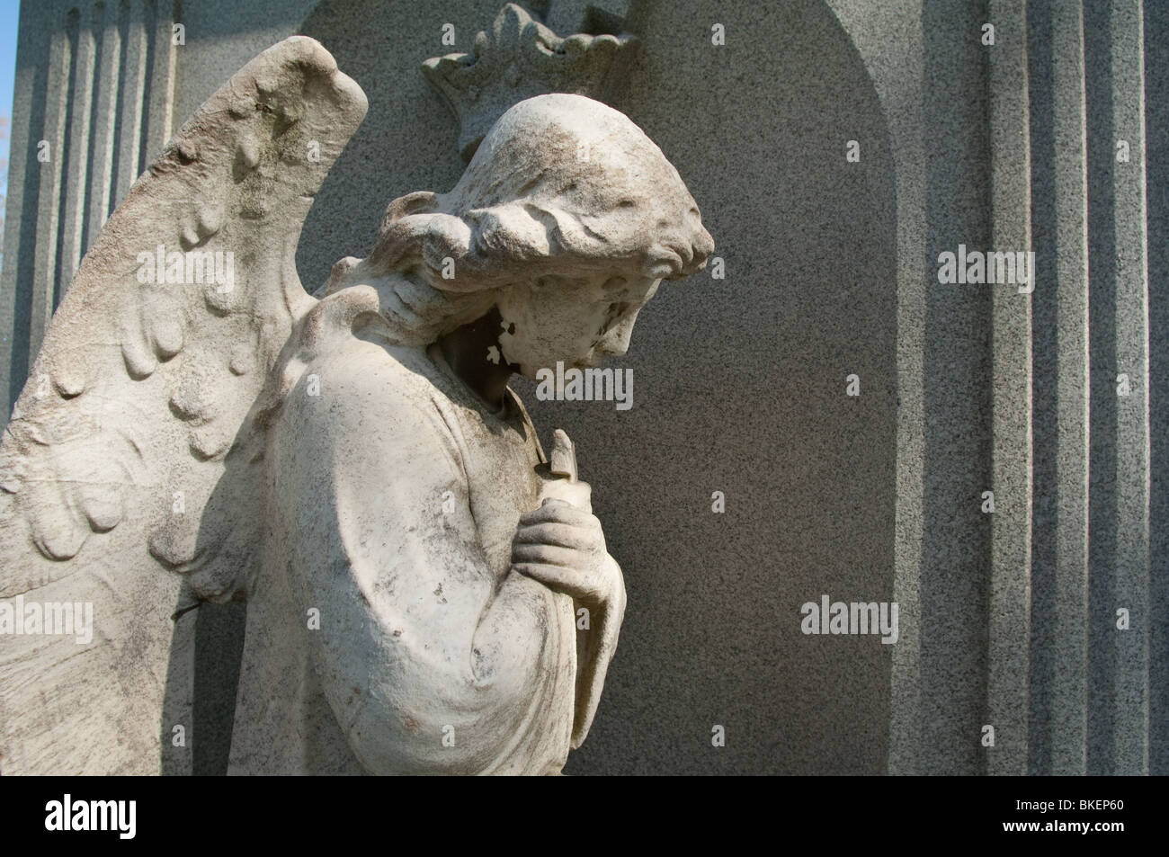 Statue of a genuflecting angel in a servile position, part of a cemetery grave marker. Stock Photo