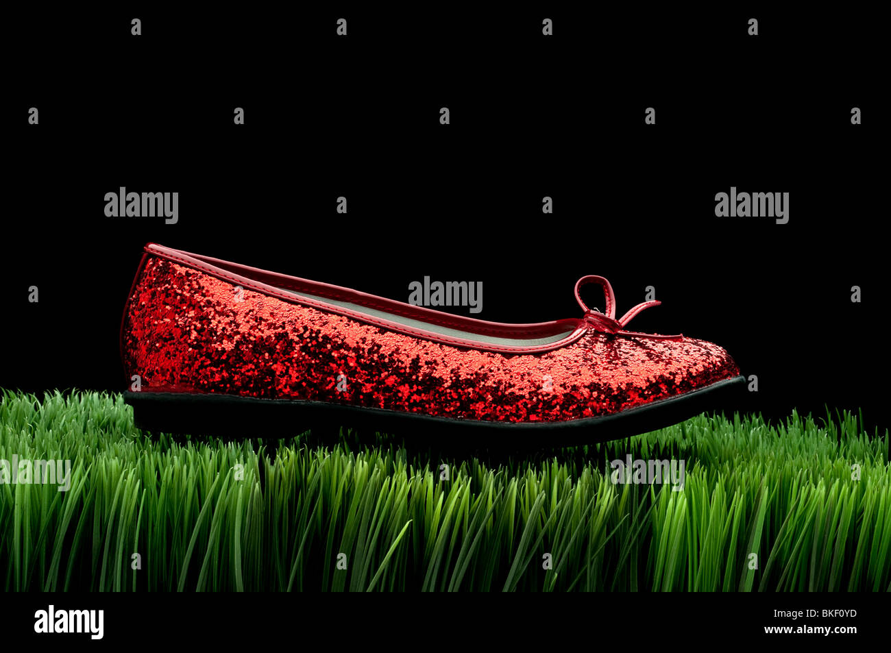 Sequined red slipper on green grass on black Stock Photo