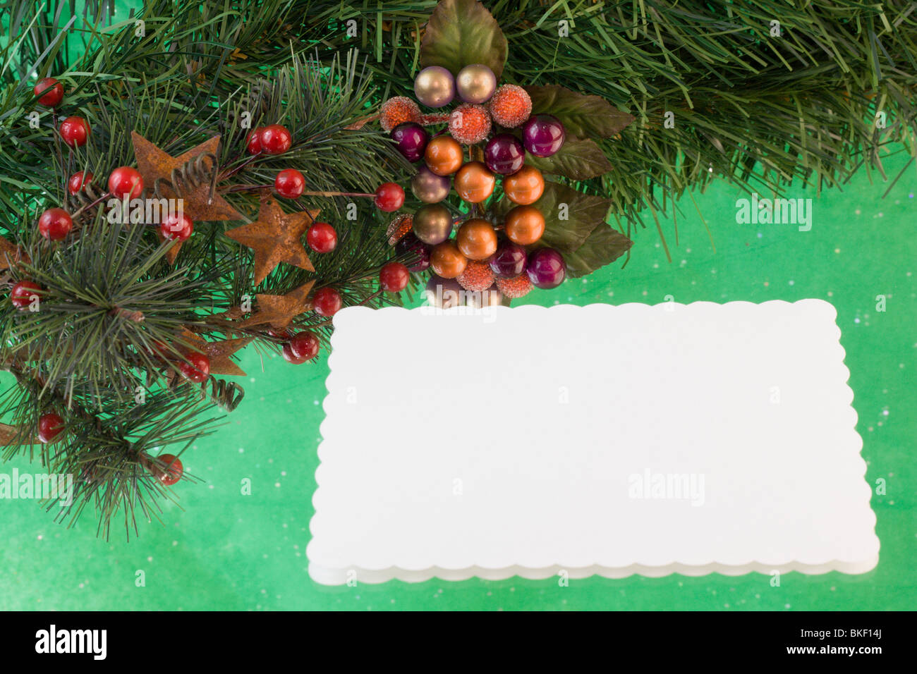 blank Christmas card with fir branch, stars, holly berries on a green reflective background with copyspace Stock Photo
