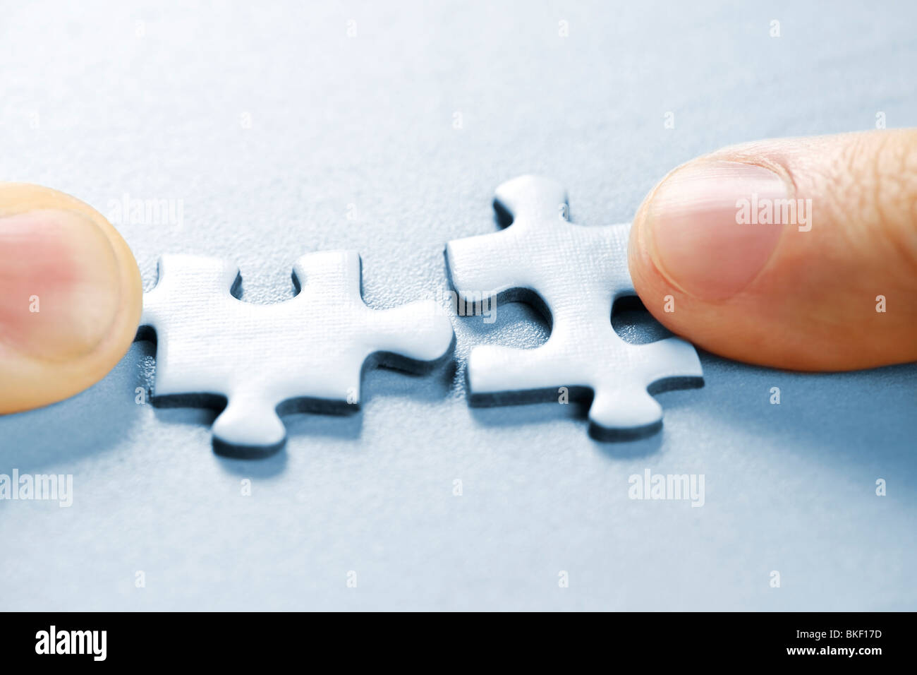 Fingers pushing two matching puzzle pieces together Stock Photo