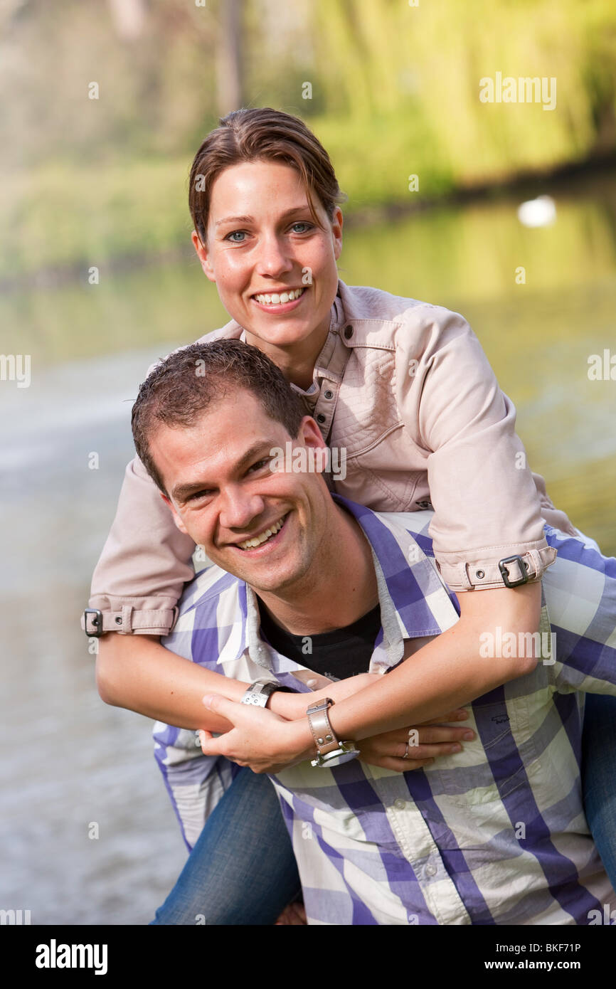 Beautiful young couple having fun doing a piggyback ride in the park ...