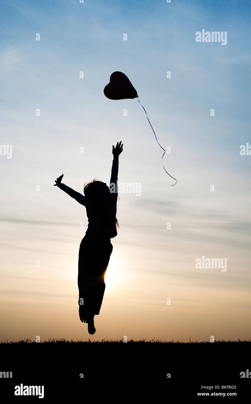 Silhouette of a young girl playing with a heart shape balloon at sunset Stock Photo