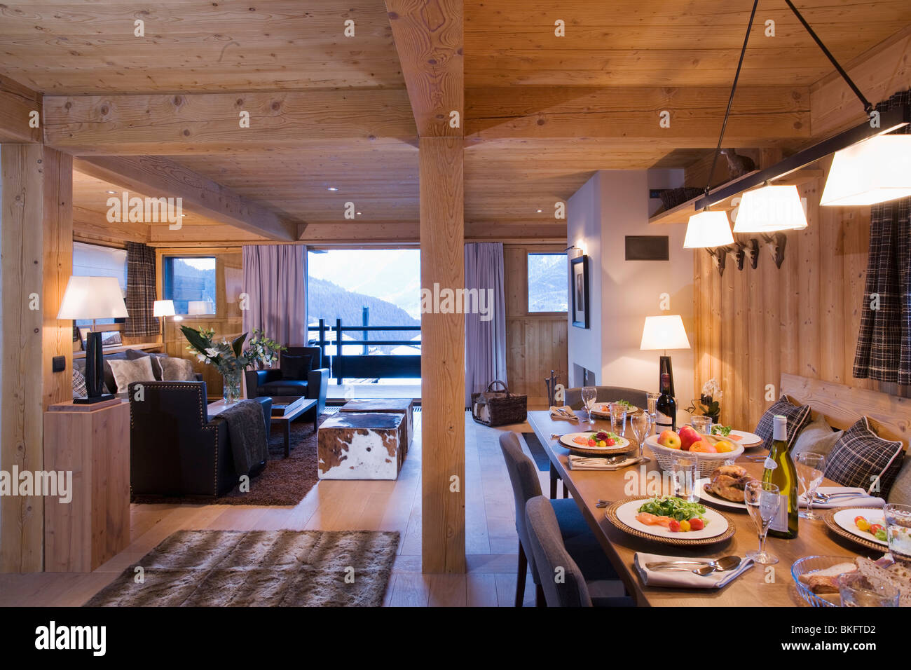Lighted lamps above table set for dinner in modern open-plan Alpine dining room and living room with view of the mountains Stock Photo