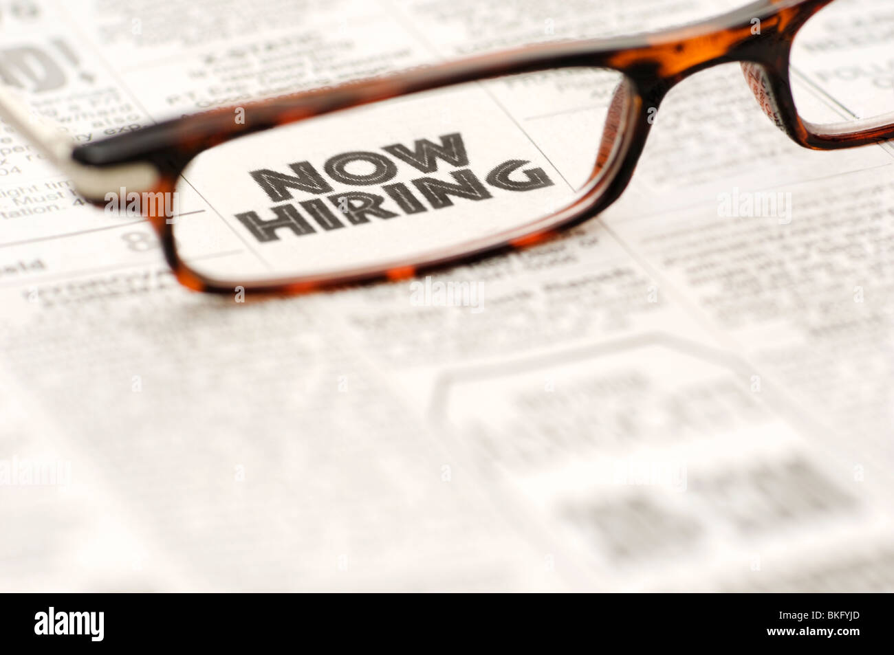 Now Hiring classified ad showing through reading glasses. Stock Photo