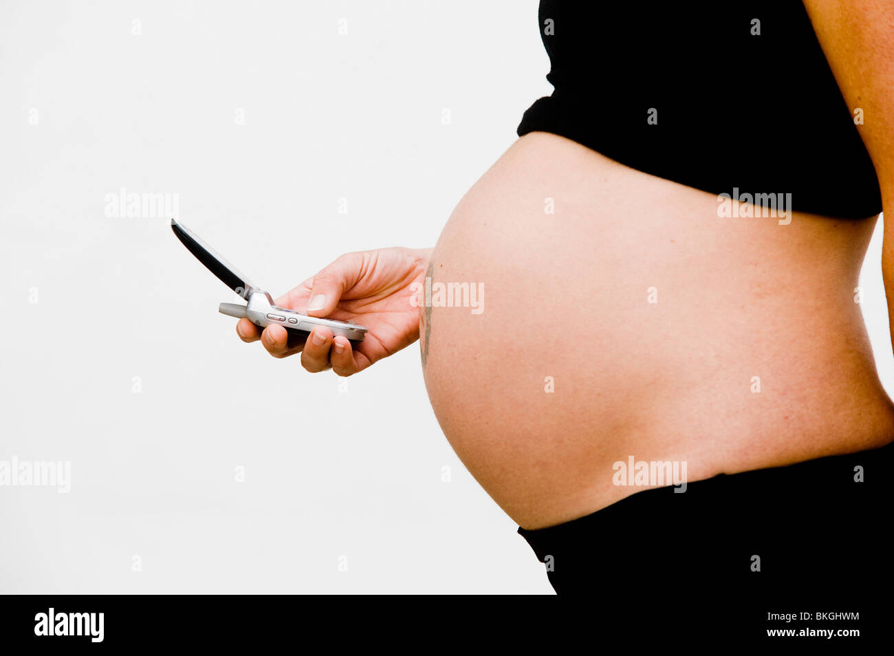 A pregnant mother makes a mobile cell phone call while holding tummy Stock Photo