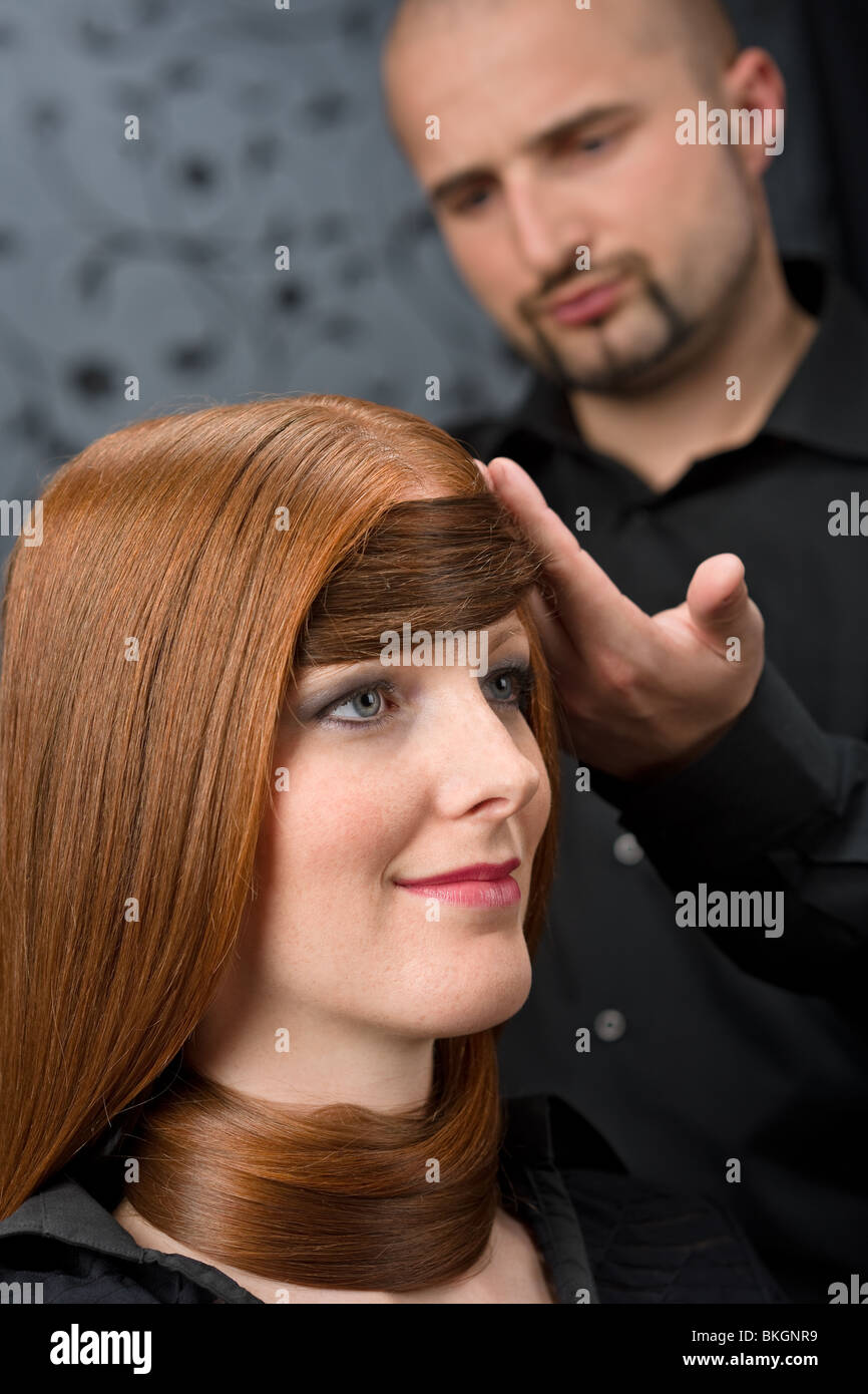 Professional hairdresser with long red hair fashion model at black