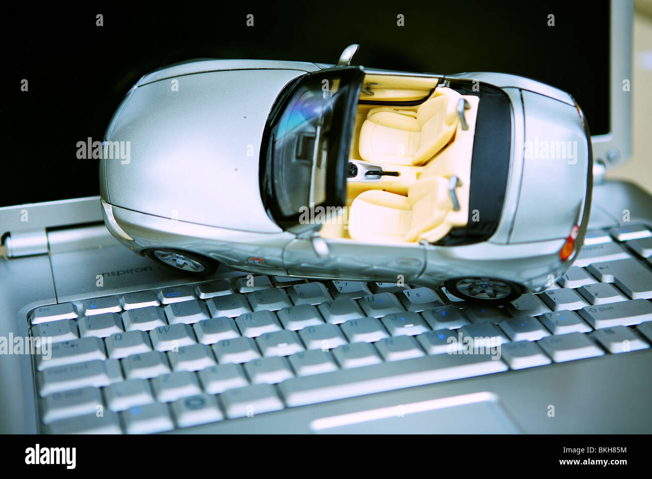 A toy BMW Z3 car on a laptop computer keyboard, representing booking a hire car online. Stock Photo