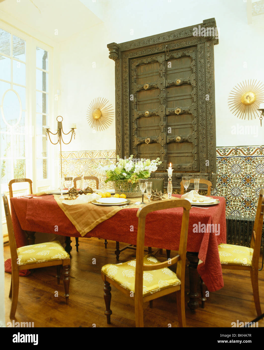 Carved doors on wall cupboard in Spanish dining room with red cloth on
