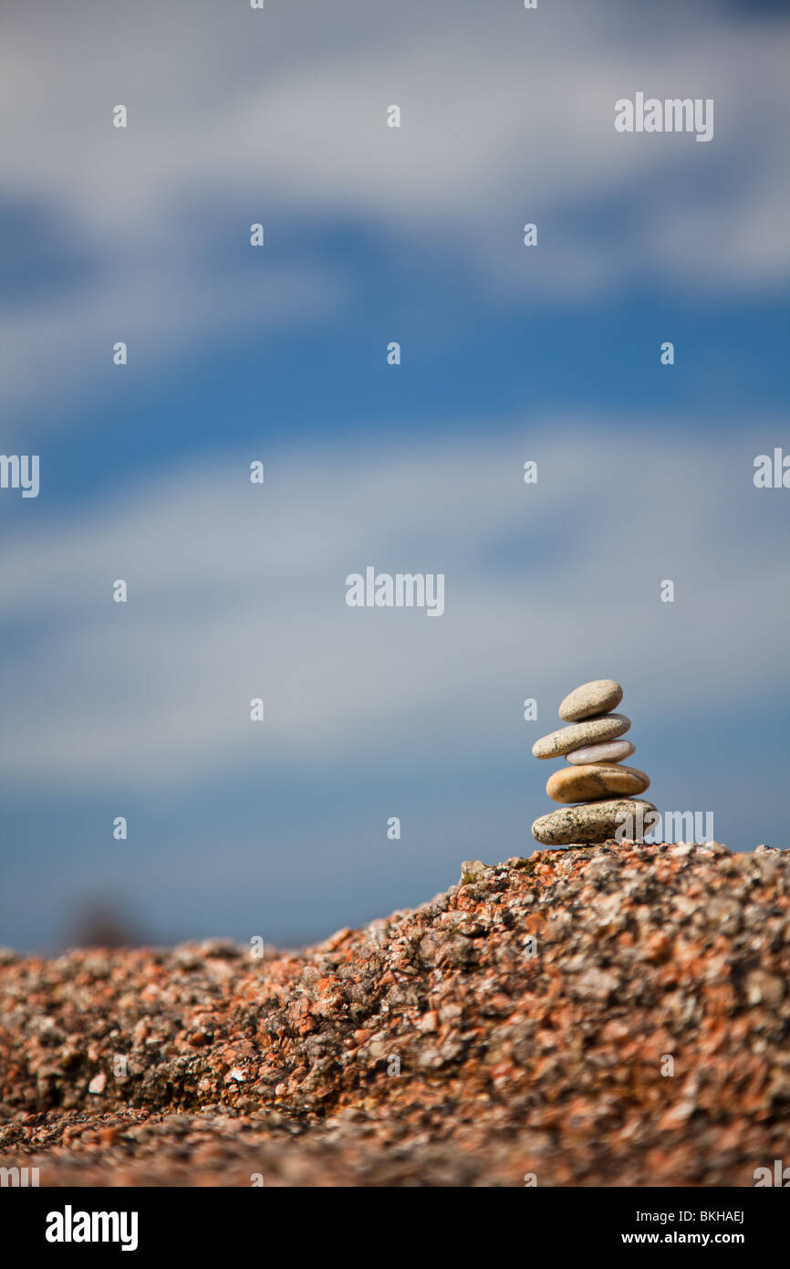 Pebbles balanced on a rock against a blue sky Stock Photo