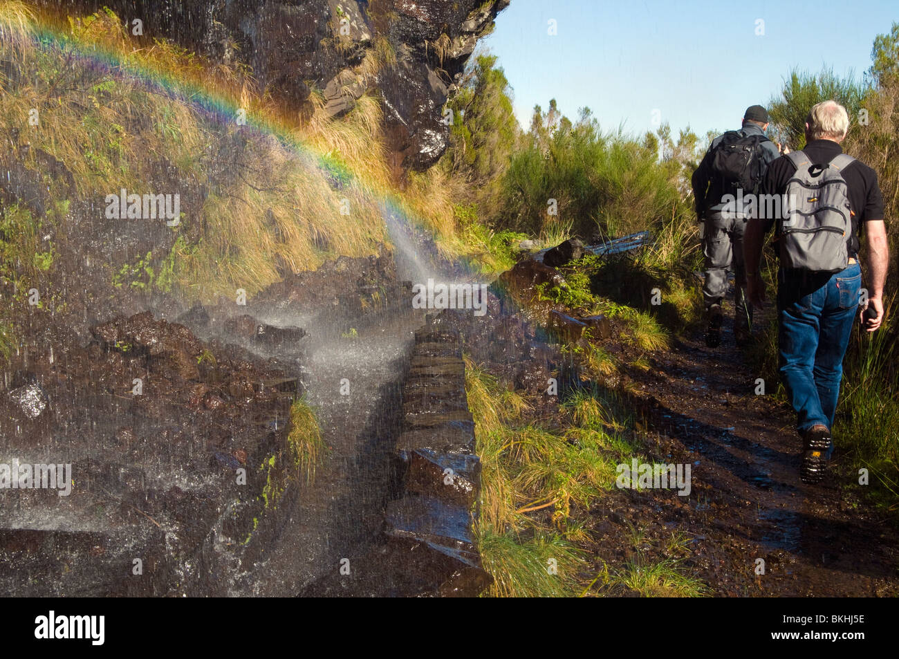 Walkers pass a rainbow where a waterfall tumbles directly into a levada (irrigation channel), Madeira Stock Photo