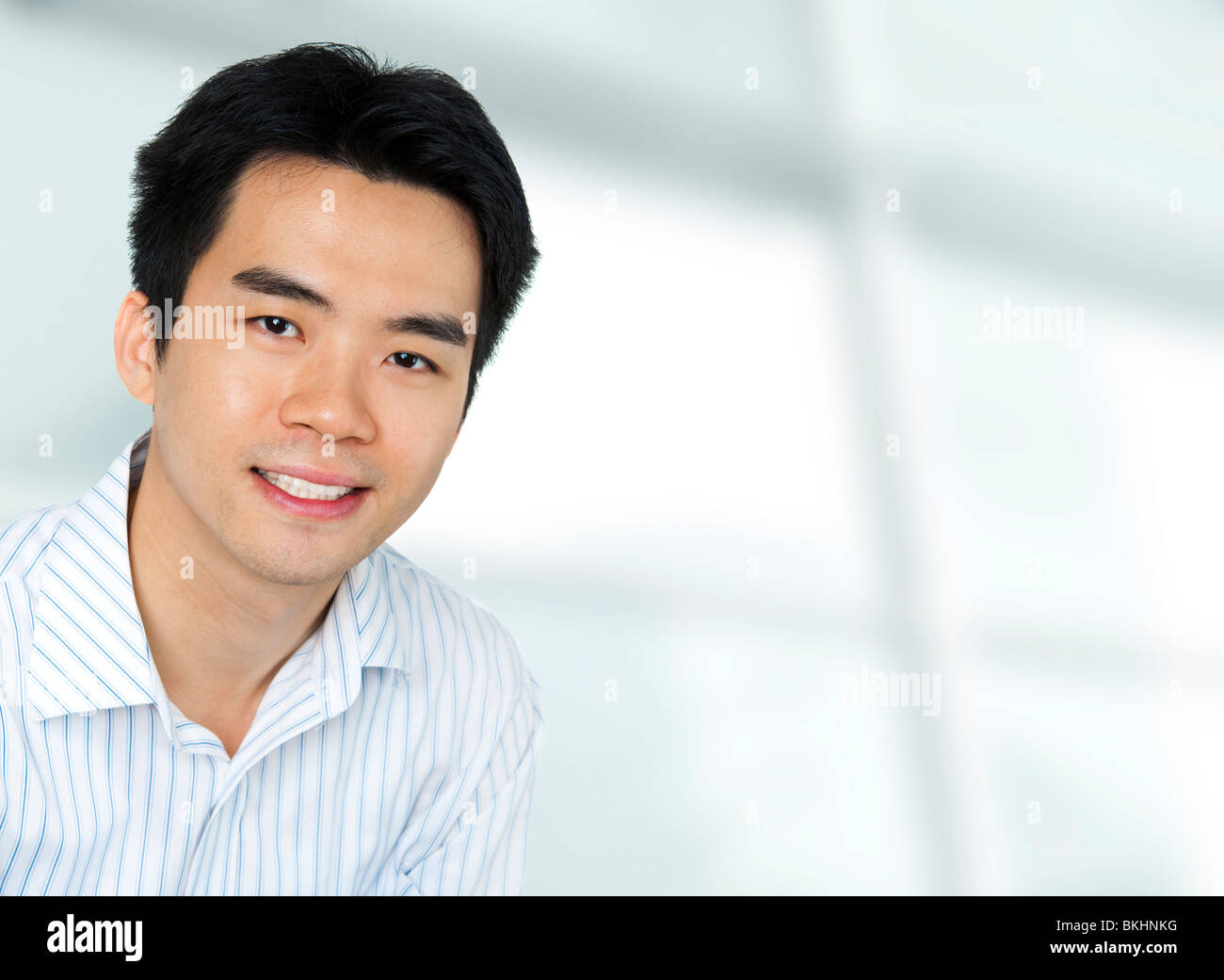 Portrait of young Asian executive in office suit, sitting in front of a modern building Stock Photo