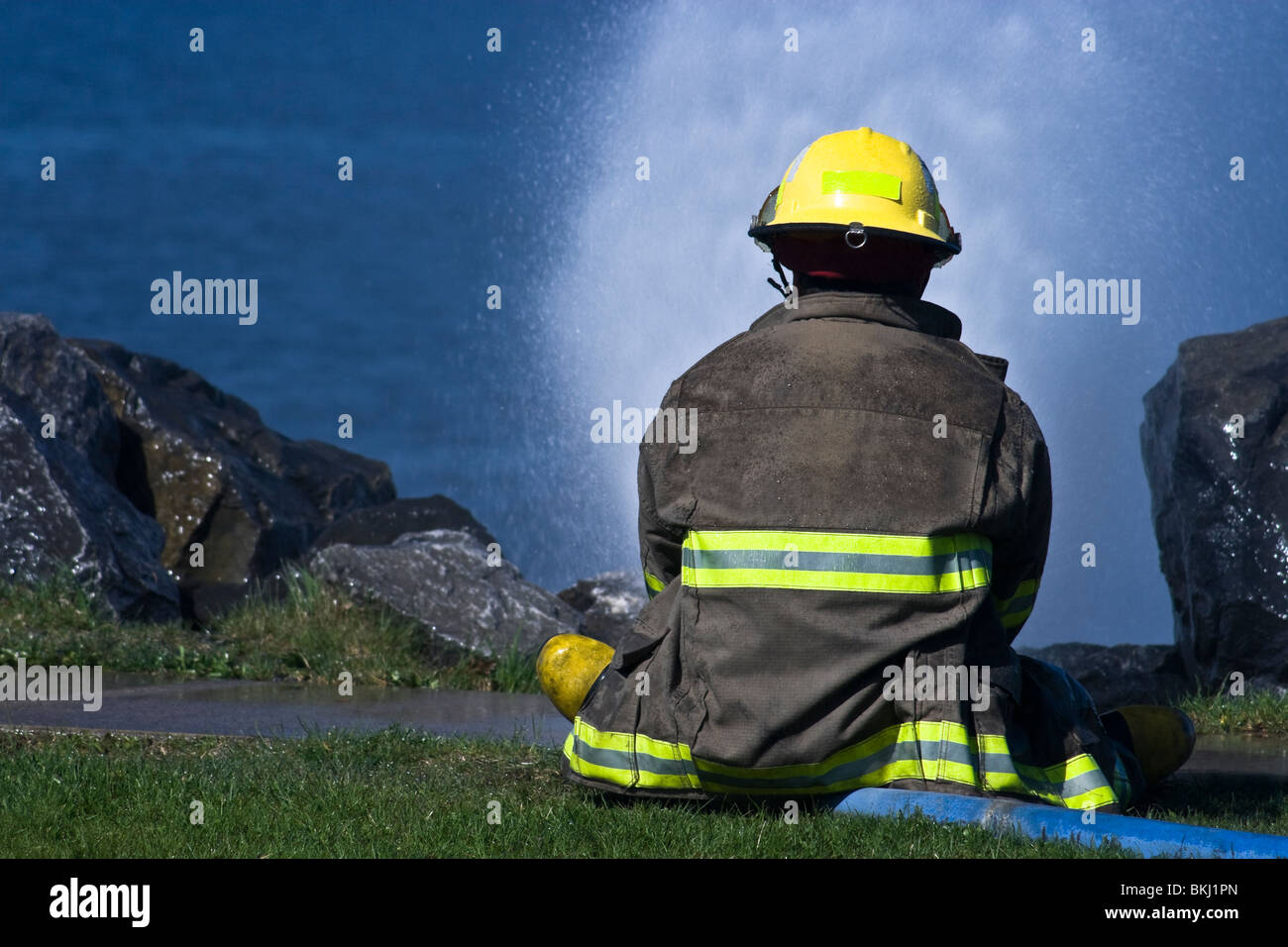 New fireman sitting on a hose under pressure Stock Photo