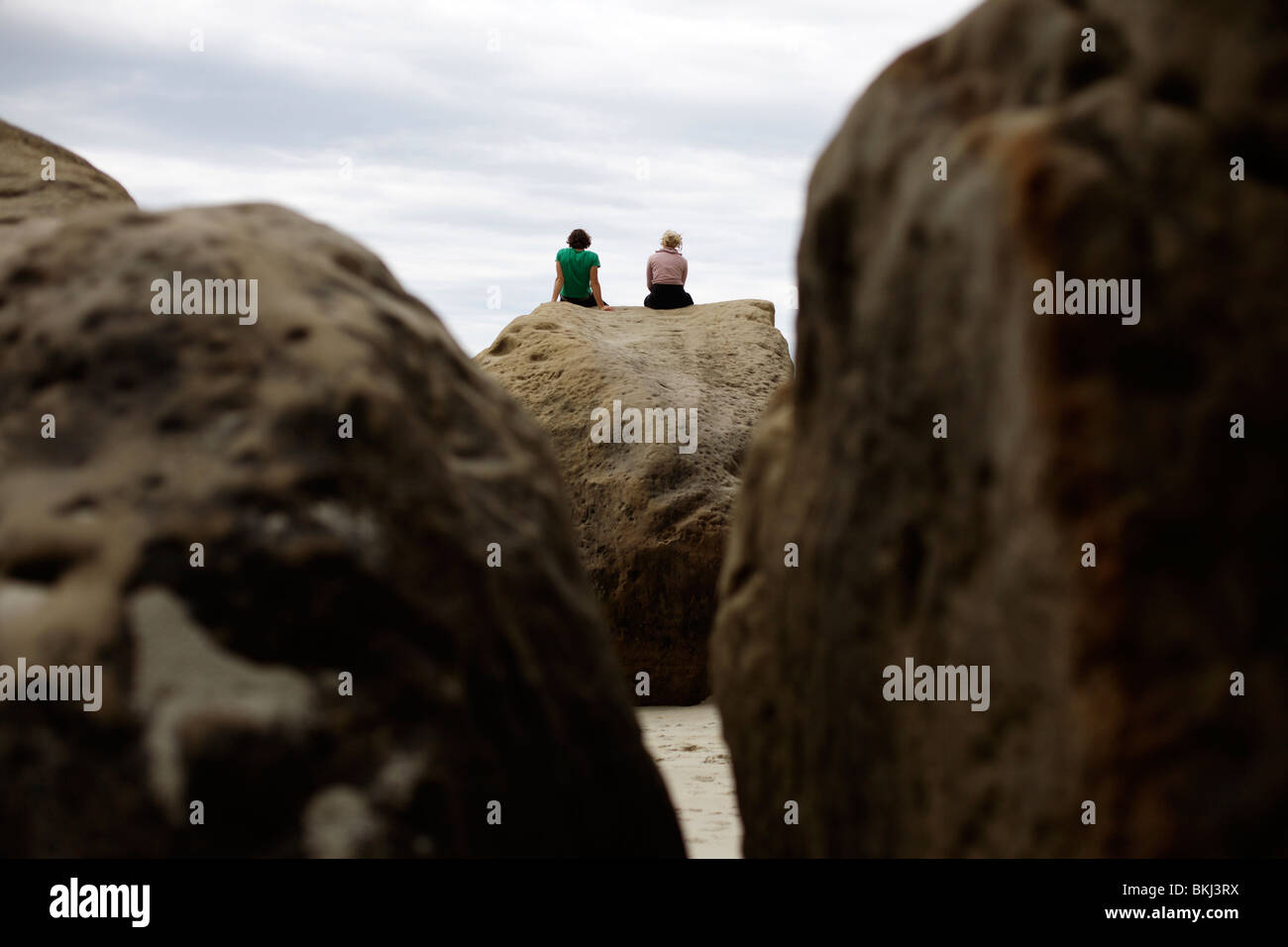 Two people sit on a rock at Tunnel Beach near Dunedin in New Zealand Stock Photo