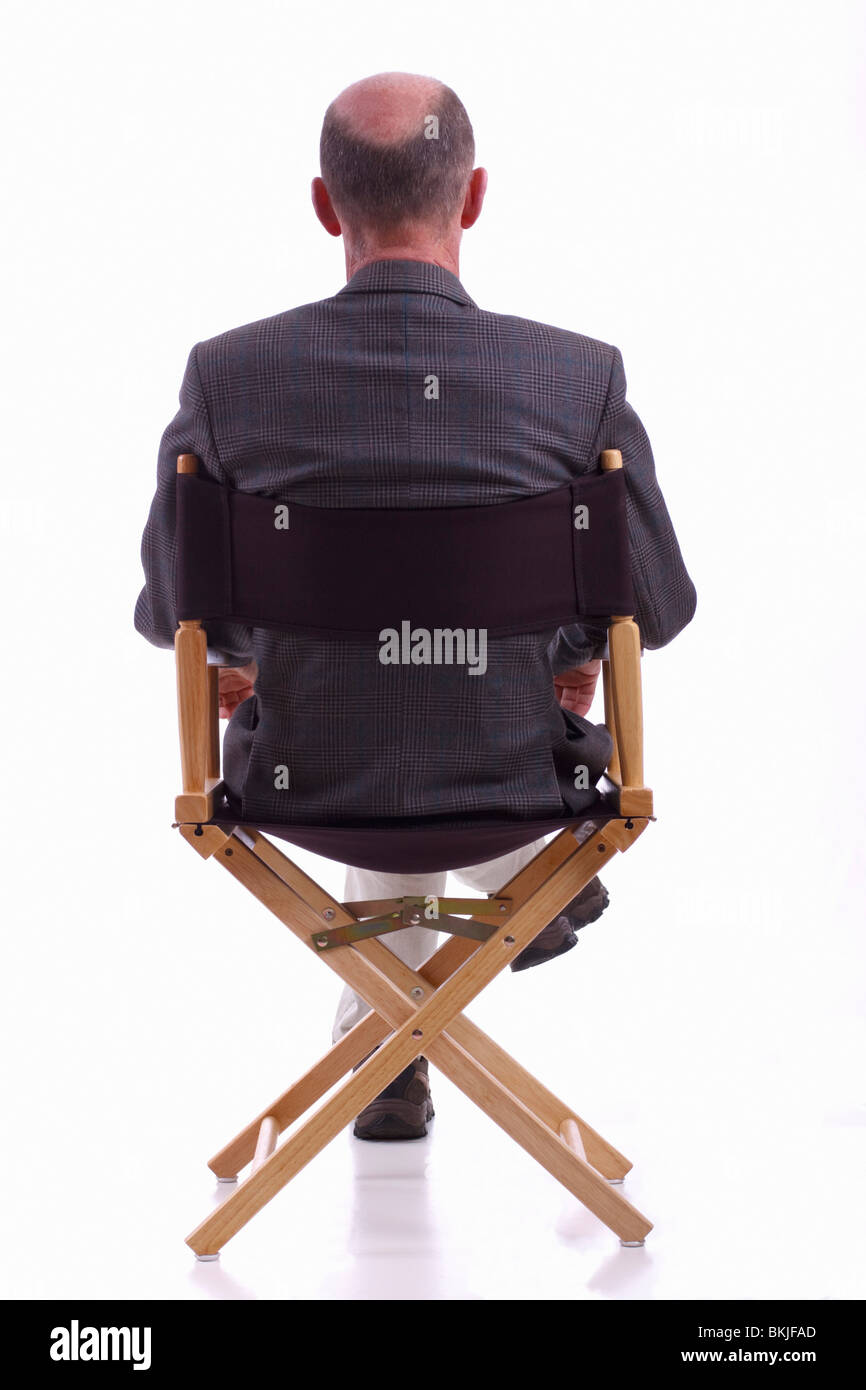 Rear view of smartly dressed mature man sitting in a directors chair. Isolated. Stock Photo