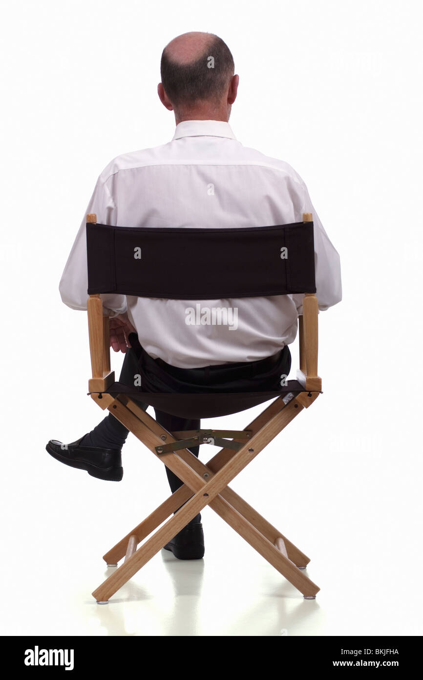 Rear view of smartly dressed mature man sitting in a directors chair. Isolated. Stock Photo