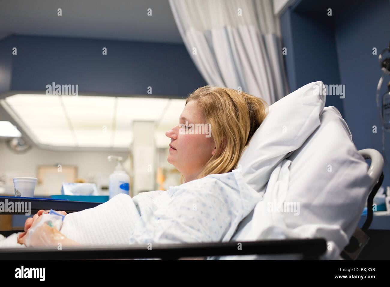 Woman recovering in a hospital room bed. Stock Photo