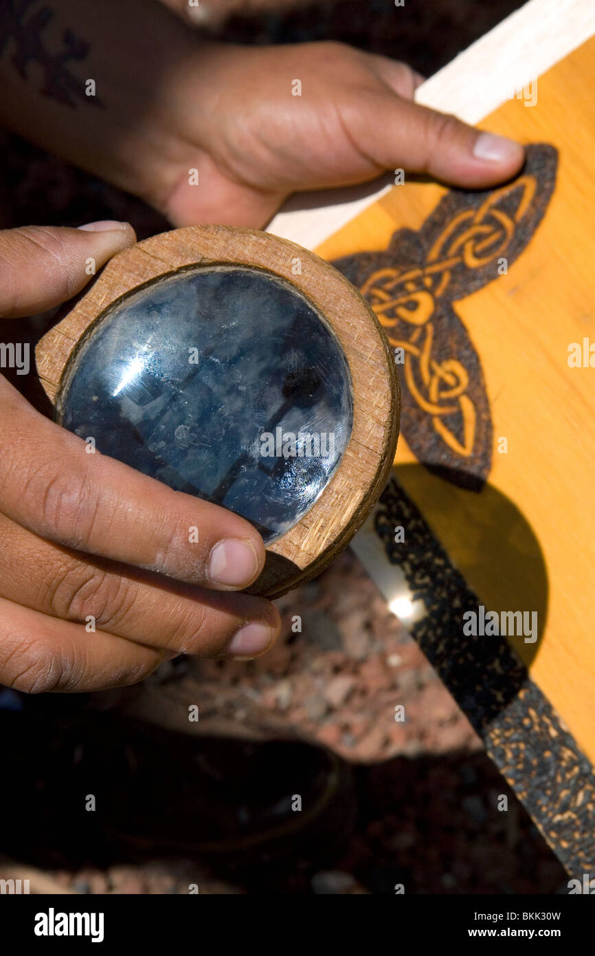 Sunlight being concentrated with a magnifying lens to burn a design into wood creating art. Cholula, Puebla, Mexico. Stock Photo