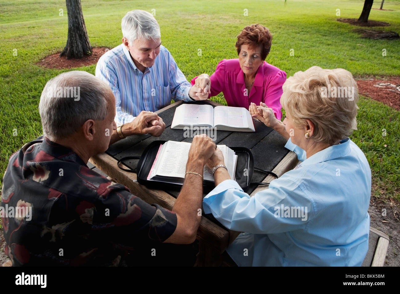 Two Couples Meeting In The Park With Their Bibles And Praying Stock Photo