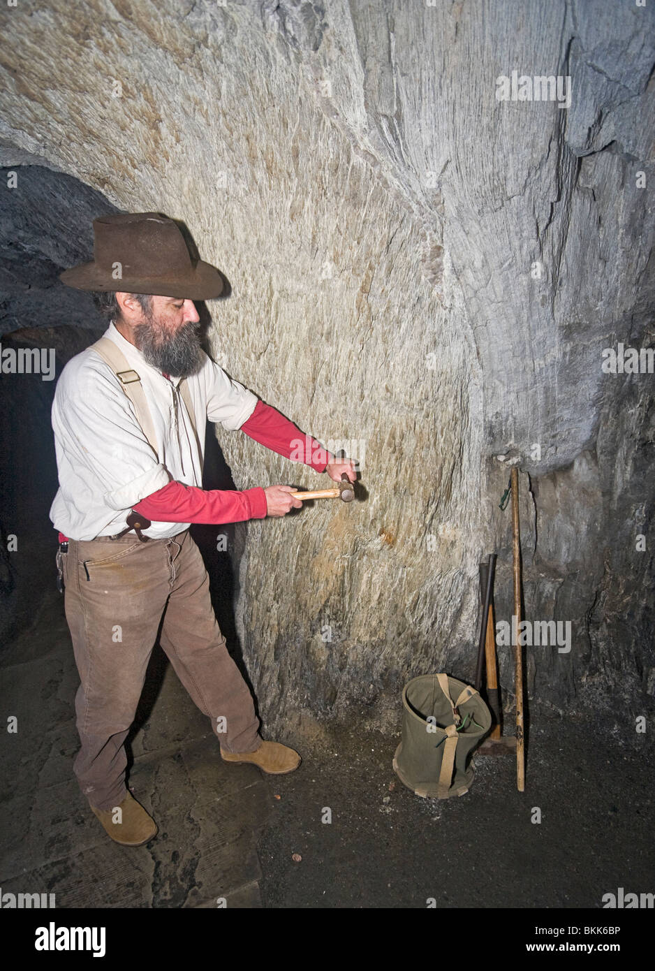 Miner drills hole for dynamite by hand to show how mining was done during gold rush days. This was known as single jacking. Stock Photo