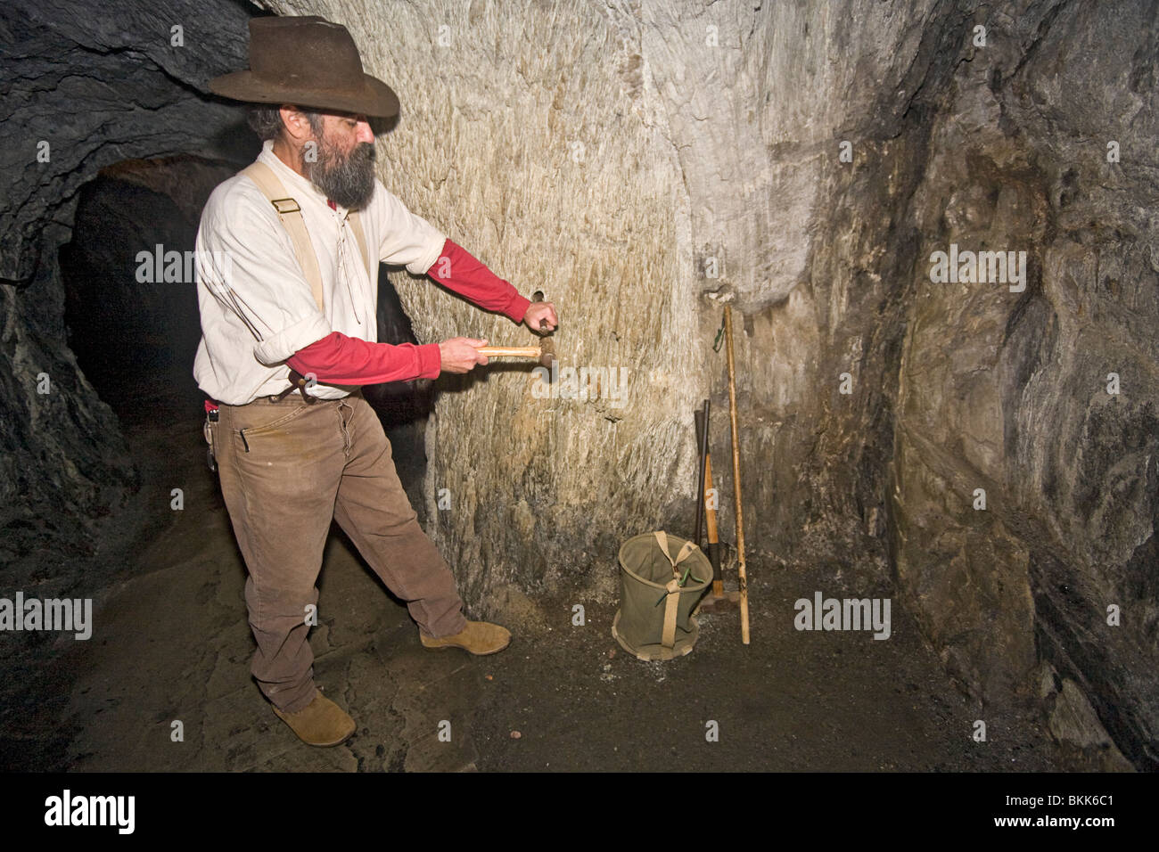 Miner drills hole for dynamite by hand to show how mining was done during gold rush days. This was known as single jacking. Stock Photo