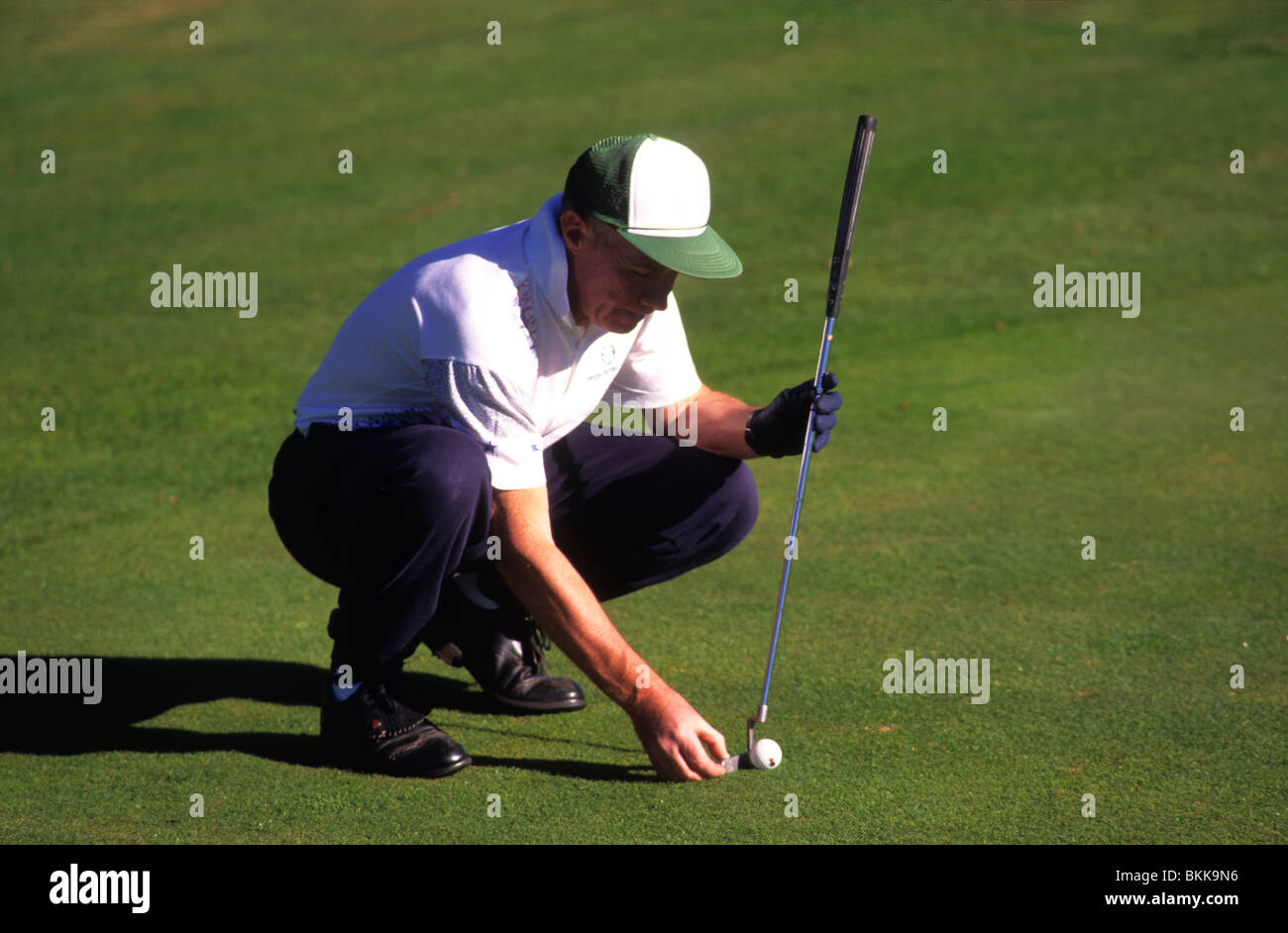 Squatted golfer aiming to put the ball into the hole. Stock Photo