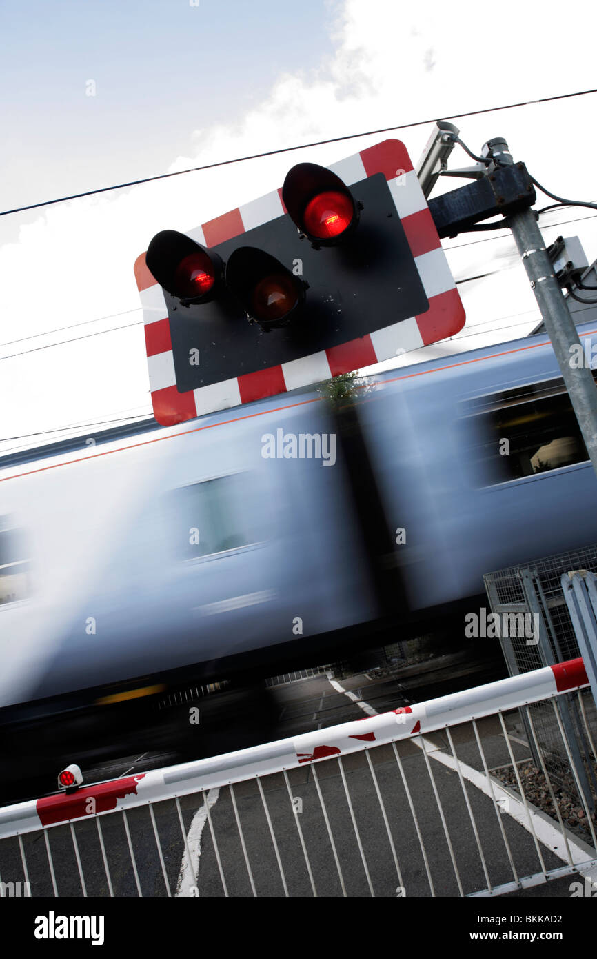 Commuter train passing a level crossing at speed with red traffic lights flashing Stock Photo