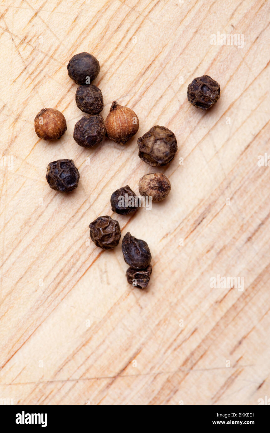 Black peppercorns (Piper nigrum) on a wooden board Stock Photo