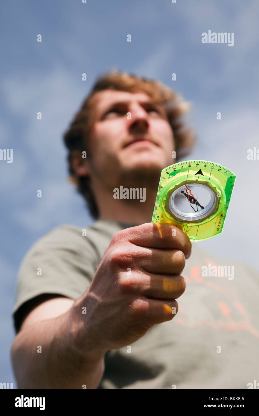 Young millennial man hiker using an orienteering compass in hand to point in right direction to go ahead looking to a positive future. England UK Stock Photo