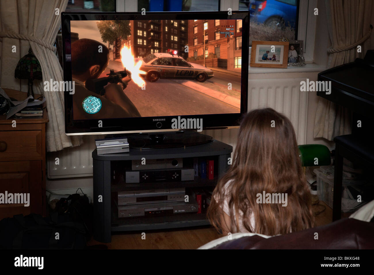 young girl playing the computer game Grand Theft Auto IV  in living room Stock Photo