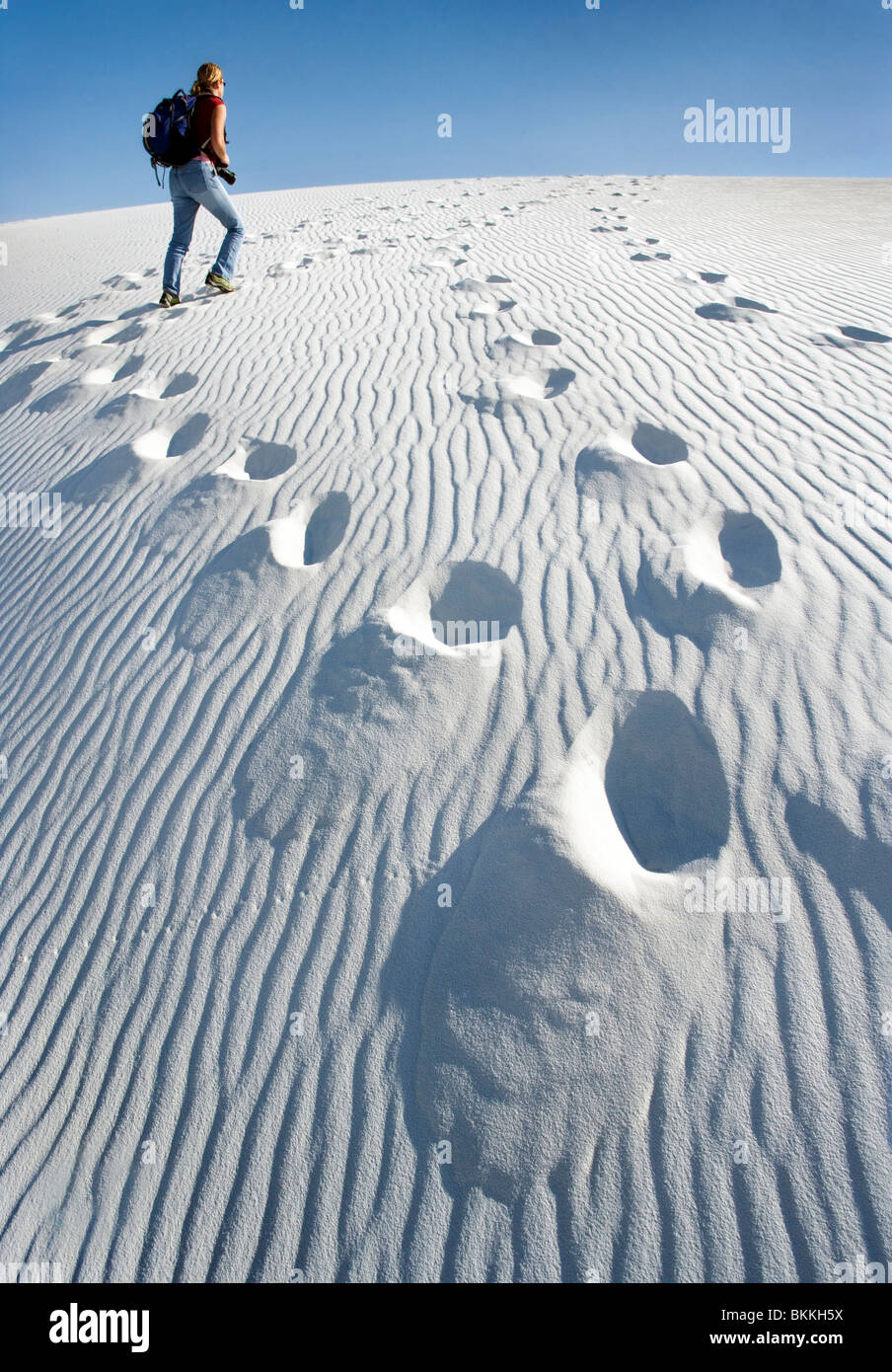 A person walking up a large white sand dune at White Sands National Monument, New Mexico. Stock Photo