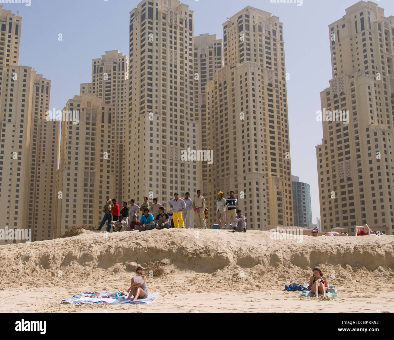 Asian migrant workers watch people relaxing on the beach in Dubai UAE Stock Photo