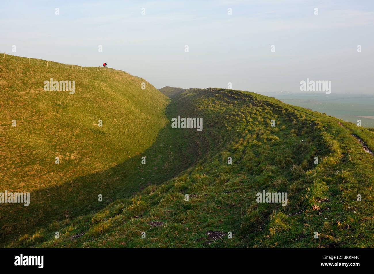 Walkers on sky line. Maiden castle Dorset at sunrise. Iron age hill fort. Stock Photo