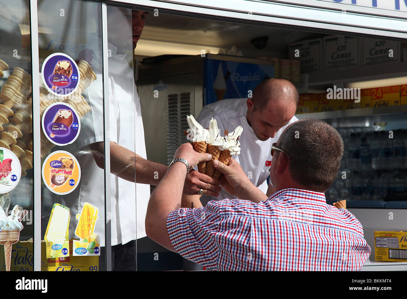 A colour image of a man buying three ice creams from a ice cream man