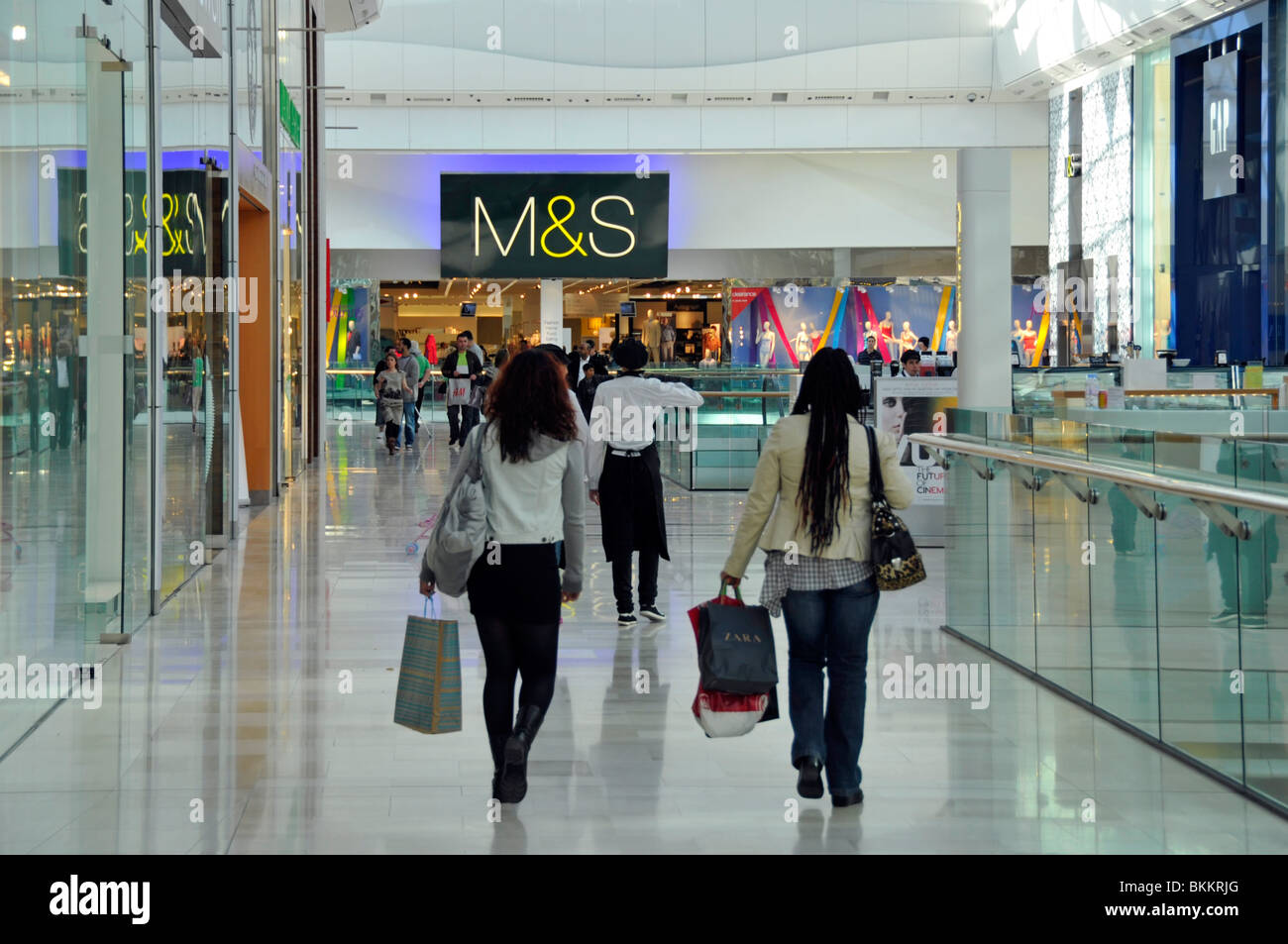Back view women shoppers walk shopping mall with Marks and Spencer retail business store in Westfield indoor shopping mall Shepherds Bush England UK Stock Photo