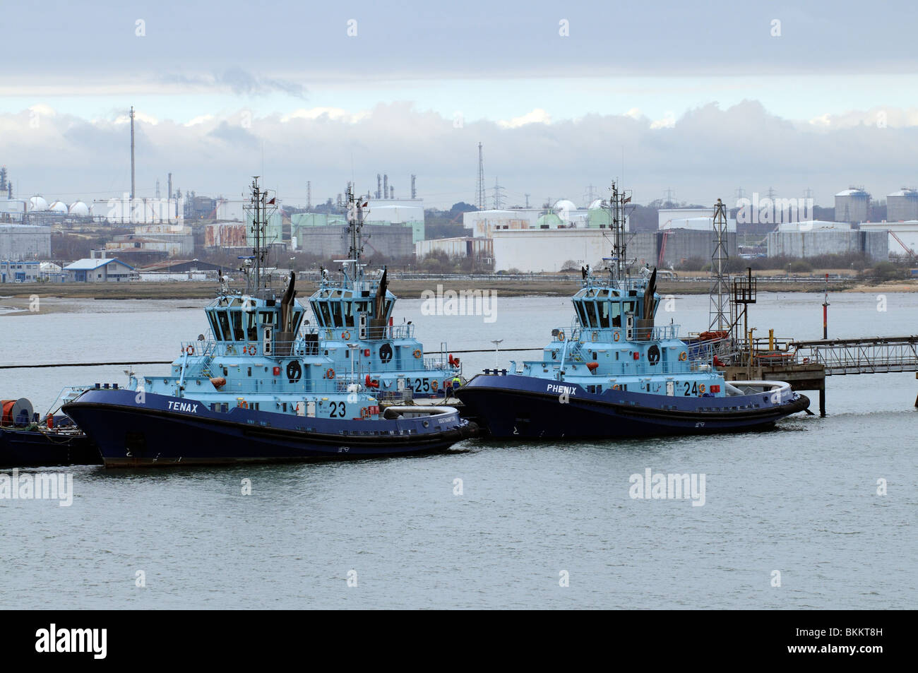 Three ocean going tugs on their moorings with a background of FMT Fawley Marine Terminal on Southampton Water southern England Stock Photo