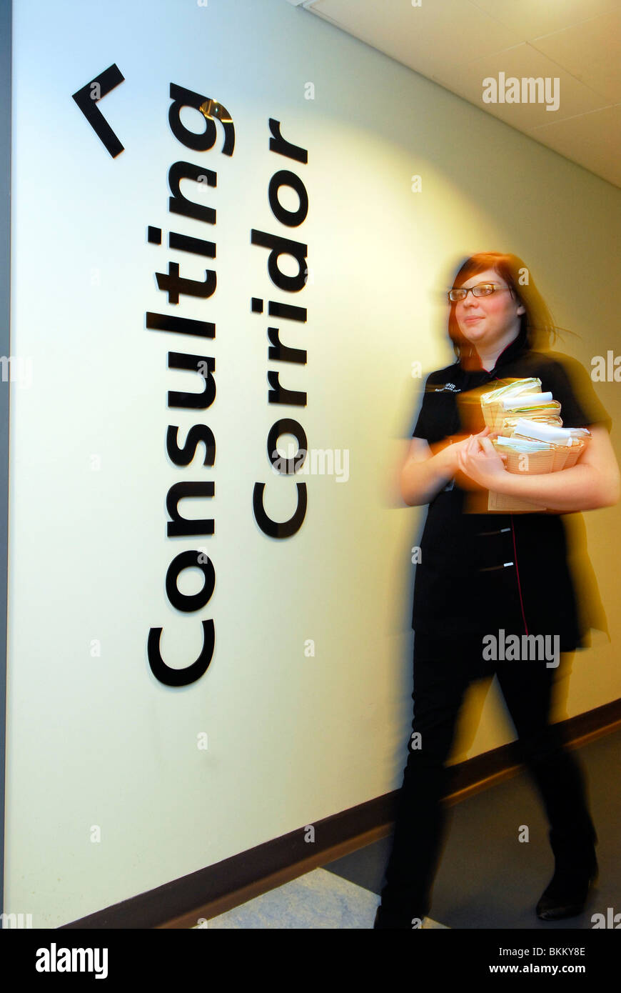 Health centre receptionist walking along corridor transporting patients' notes, Barnsley, Yorkshire, UK. Stock Photo