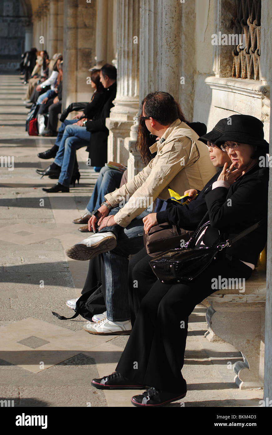 Tourists sit on benches in St Mark's Square, venice, Italy Stock Photo