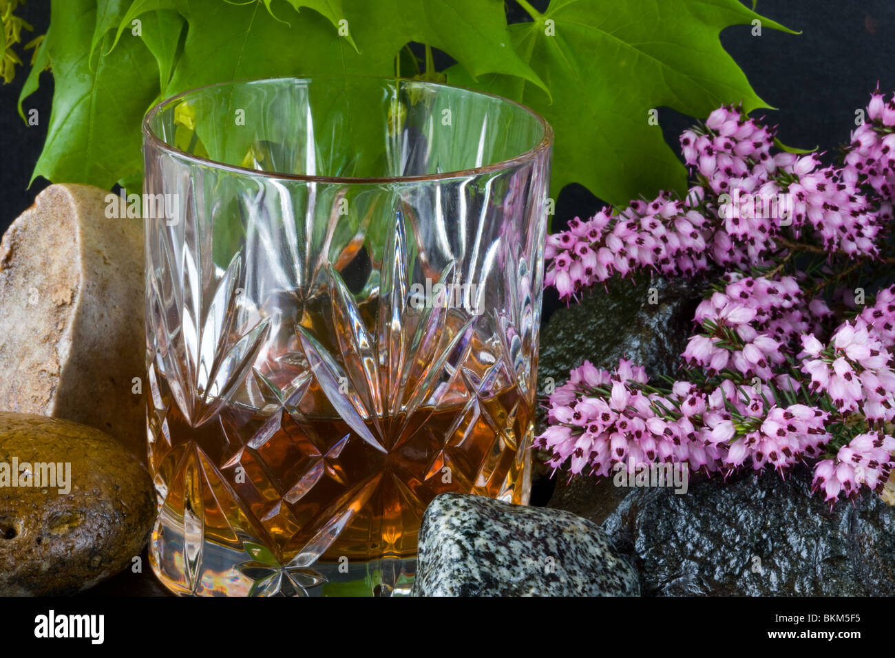 A glass of whisky on rocks with heather and leaves Stock Photo
