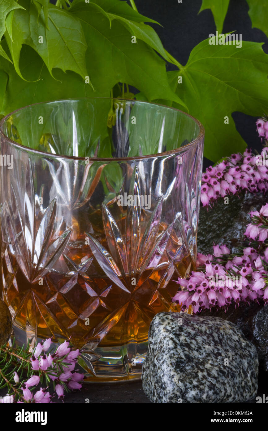 A glass of whisky on rocks with heather and leaves Stock Photo