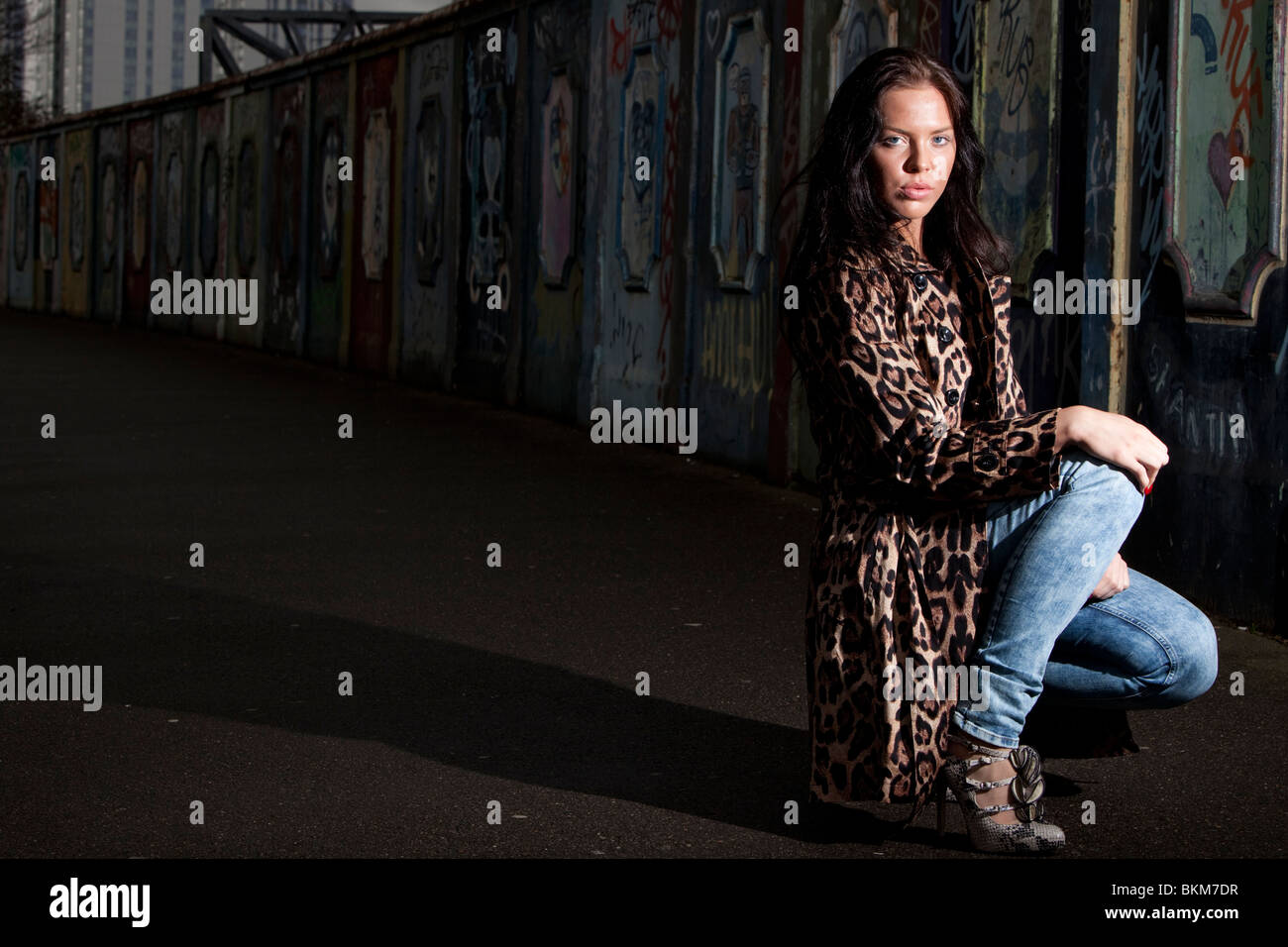 Portrait of a young woman kneeling by a wall Stock Photo