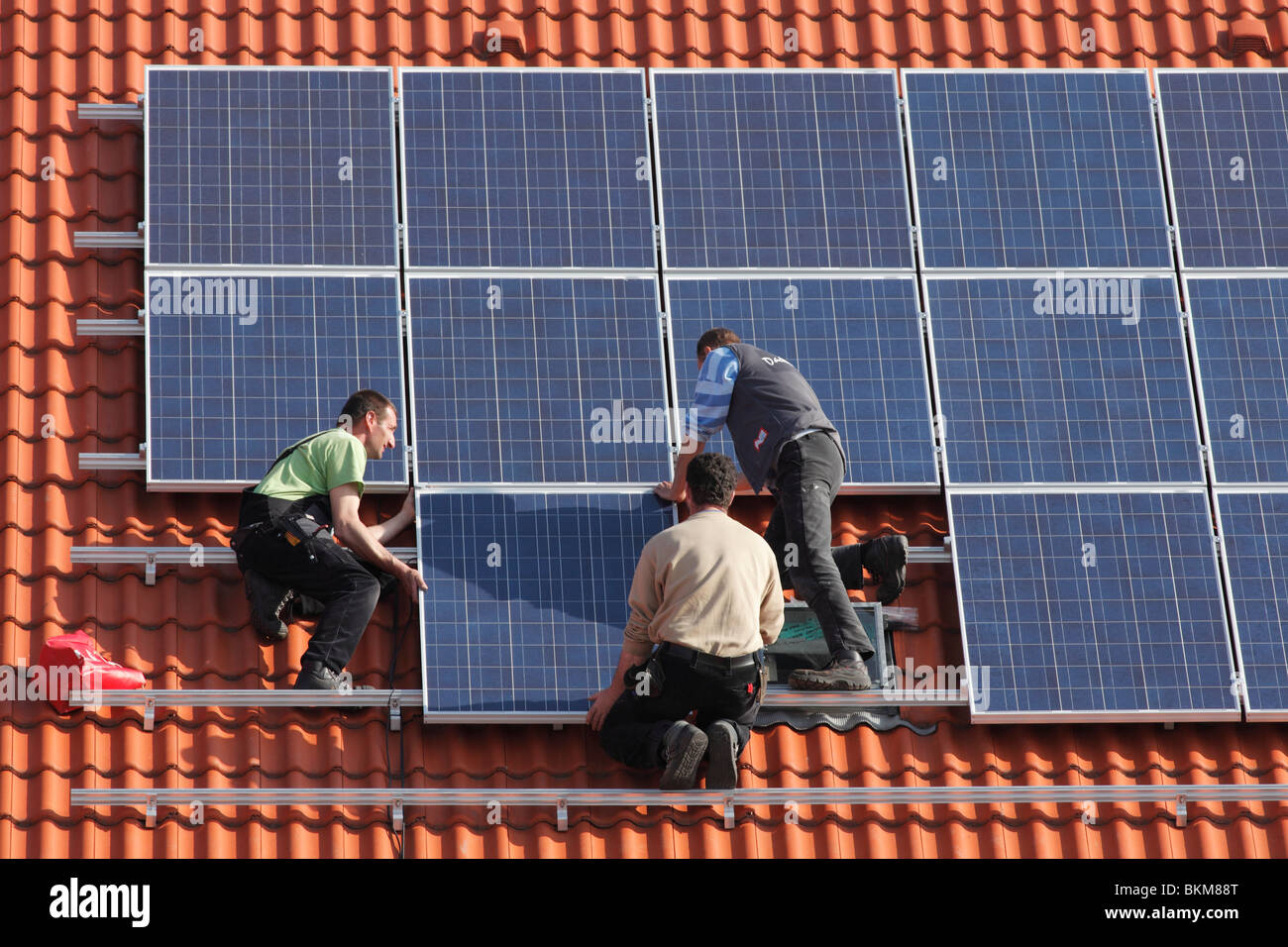 Workmen installing solar panels on a roof Stock Photo