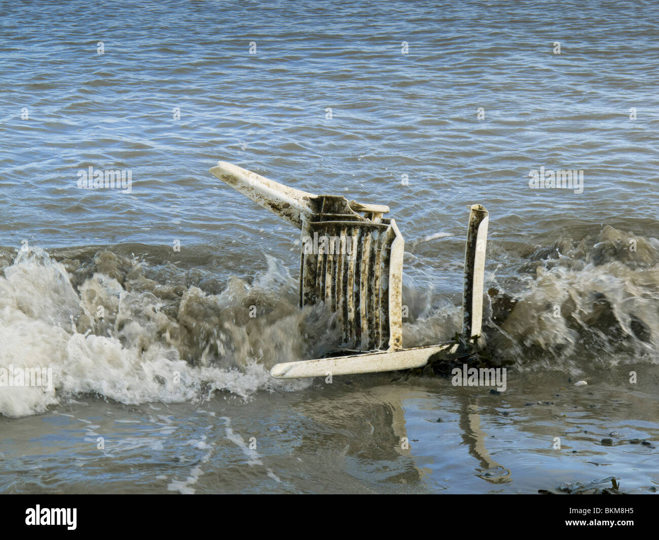 A dumped broken plastic garden chair in the sea on the beach at