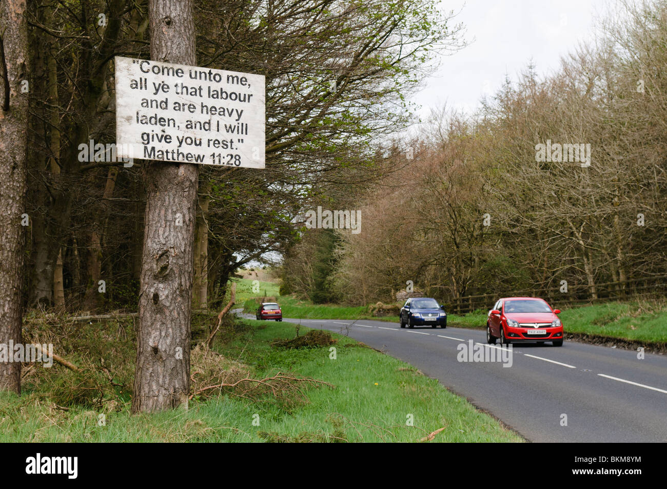 Sign with a bible verse nailed to a tree by the side of a road with traffic Stock Photo